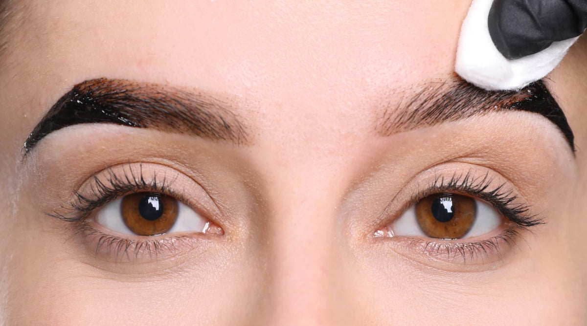 Applying brow henna while cleaning excess pigment to define the eyebrow shape.